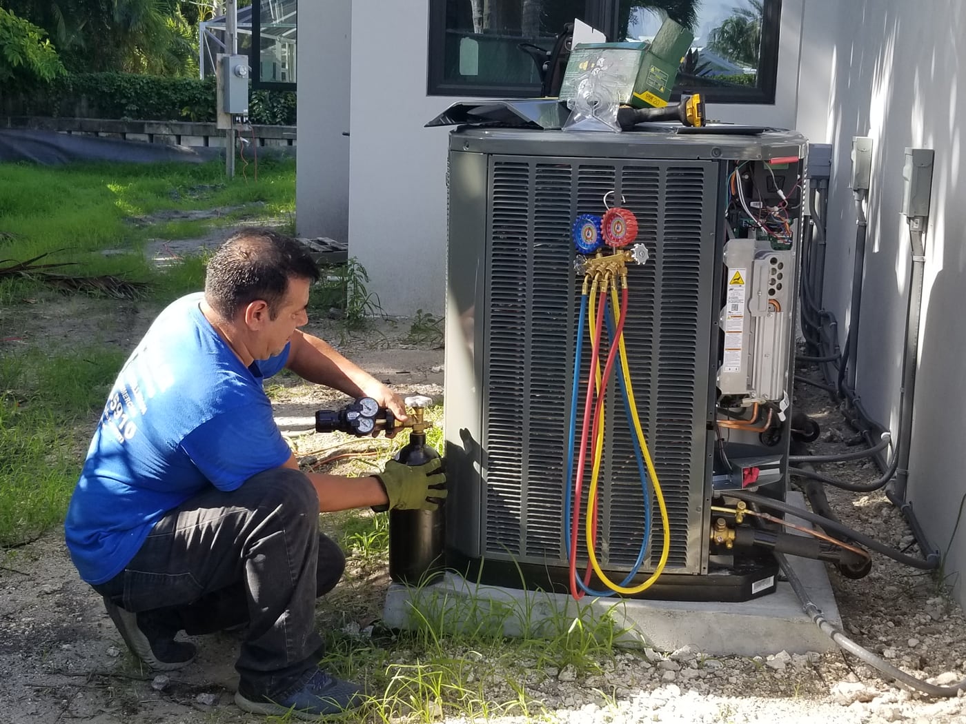 Jireh Cooler technician performing hands-on maintenance work on a residential outdoor air conditioning unit